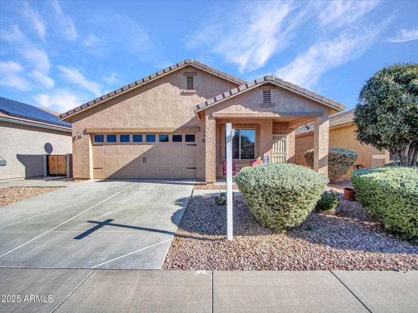 This inviting Buckeye home showcases low-maintenance desert landscaping, a covered front porch, and a clean driveway, highlighting energy-efficient design and welcoming curb appeal perfect for Arizona living.