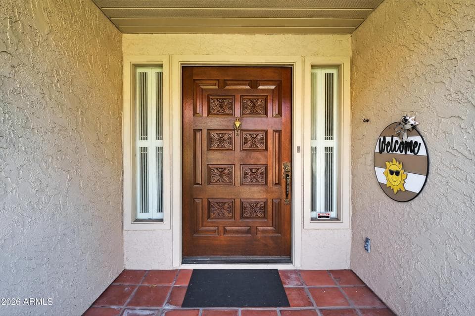 A distinctive wood front door with decorative carved details and narrow sidelights creates a warm welcome to this Scottsdale residence. The sheltered entry and Saltillo-style tile flooring add character while providing a memorable first impression.