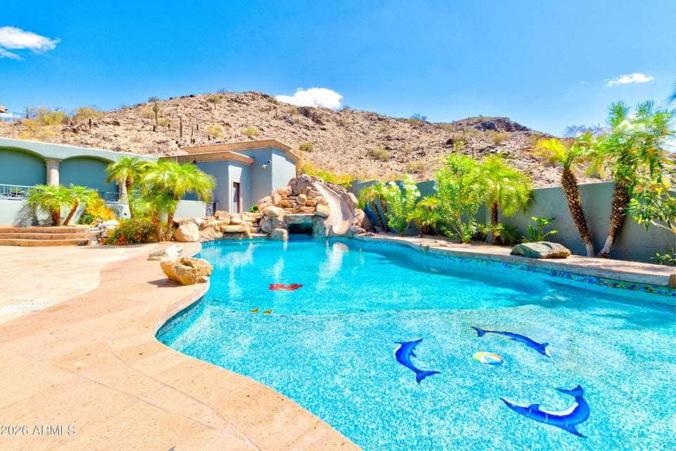 Resort-style pool with rock waterfall and scenic desert hillside views.
