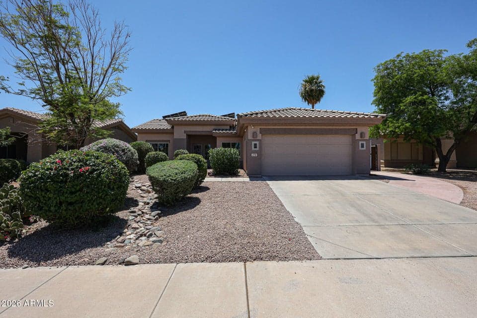 Title: Landscaped Goodyear Exterior Description: Welcoming front exterior of this Goodyear property featuring mature desert landscaping, a tile roof, two-car garage, wide driveway, and low-maintenance gravel yard. Solar panels are also visible above the roofline, highlighting the home's energy-conscious design.