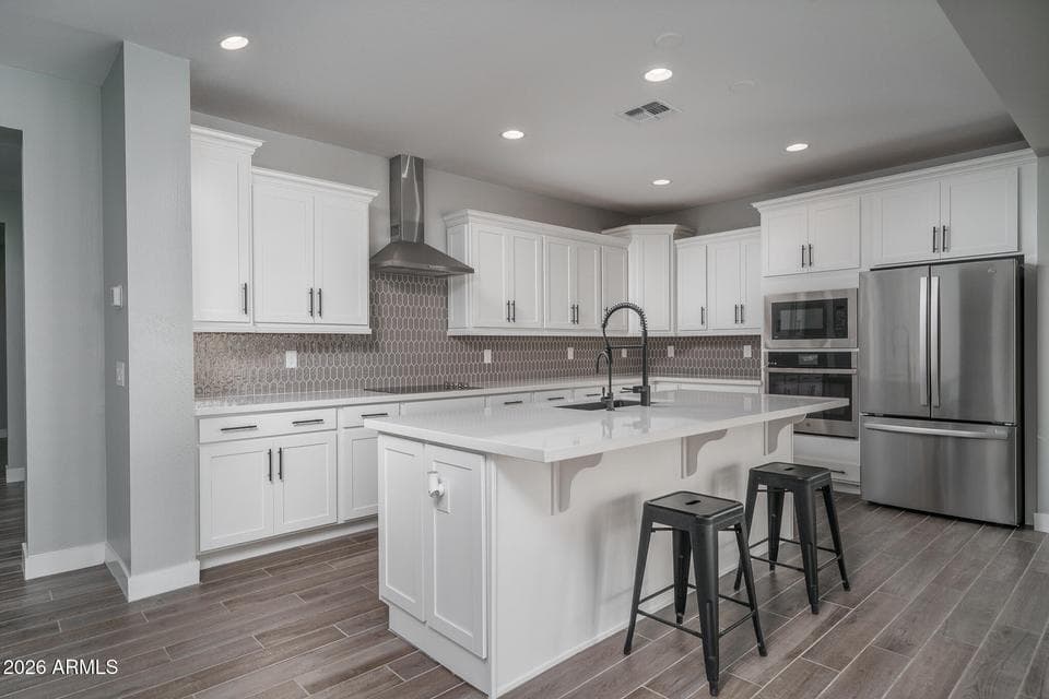 Beautiful gourmet kitchen featuring crisp white cabinetry, quartz countertops, an oversized island with breakfast bar seating, stainless steel appliances, designer backsplash, and abundant storage. This modern kitchen is the heart of this move-in-ready home in Surprise, offering the perfect blend of style and functionality for entertaining and everyday living.