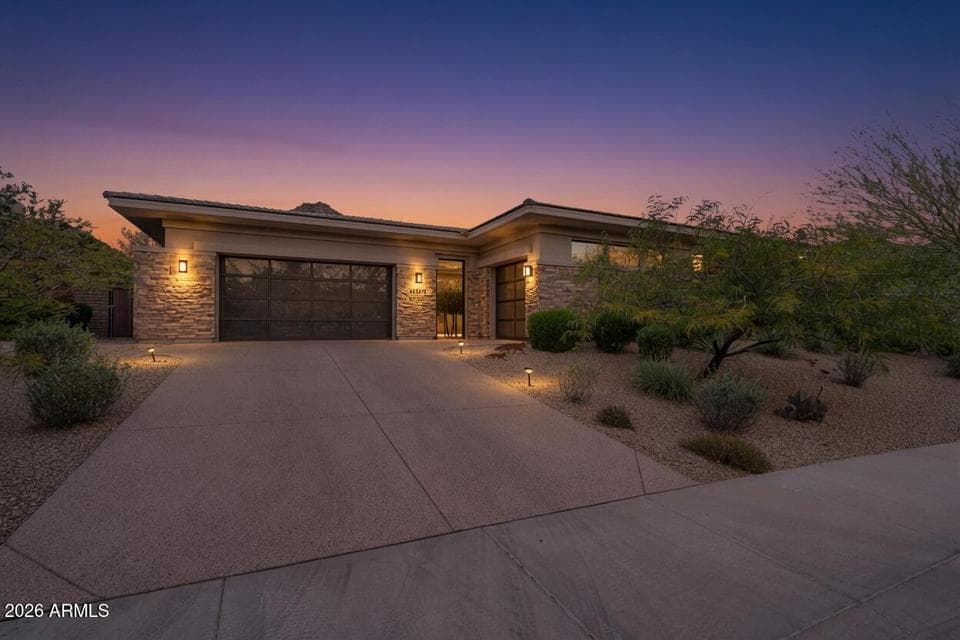 Welcome home to this stunning modern retreat. Warm stone veneer and a glass front door invite you in, while lush desert landscaping and soft pathway lighting create a peaceful entry. The perfect place to unwind under a breathtaking Arizona sunset.