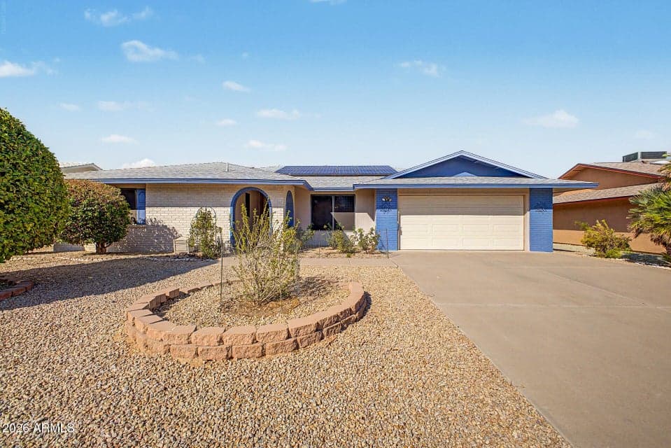 Attractive curb appeal with a spacious driveway, desert landscaping, mature trees, and a welcoming covered entry.