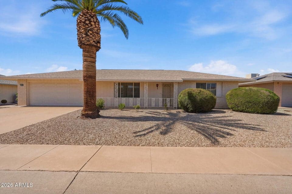 Attractive front elevation showcasing mature palm trees, low-maintenance desert landscaping, a covered front porch, and timeless curb appeal that welcomes you home to this move-in-ready Sun City property.