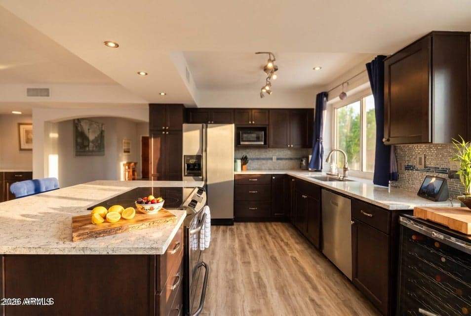 Chef's kitchen features a large kitchen island, quartz countertops, custom cabinetry, and stainless steel appliances, plus a built-in wine refrigerator. This renovated Scottsdale home offers an open floor plan filled with natural light, perfect for entertaining or everyday living.