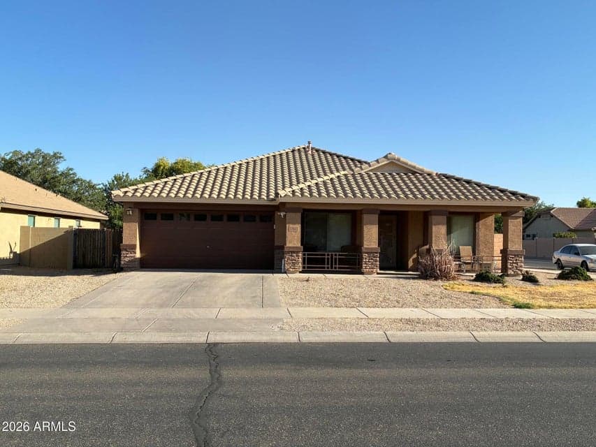 Front exterior of this single-level Surprise home featuring a tile roof, two-car garage, covered front patio, stone-accented columns, and low-maintenance desert landscaping. The welcoming streetscape and generous covered entry create an attractive introduction to this 3-bedroom-plus-den property.
