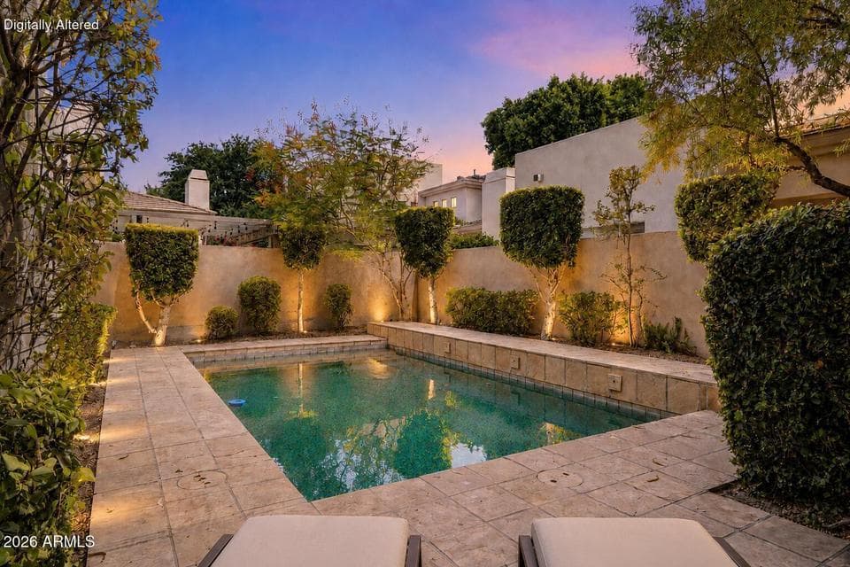 An illuminated private pool creates a serene backyard oasis at this Gainey Village Casitas property in Scottsdale. Mature landscaping, accent lighting, tiled decking, and a secluded setting showcase resort-style outdoor living ideal for relaxing or entertaining beneath dramatic desert skies.