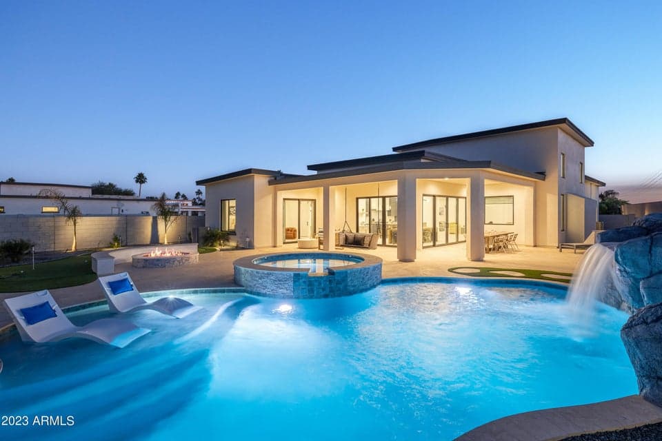 Stunning private backyard with putting green, cornhole, porch swing, covered lounge area, covered dining area, fire pit, built-in BBQ grill, and sparkling pool featuring in-pool loungers and a waterslide grotto.