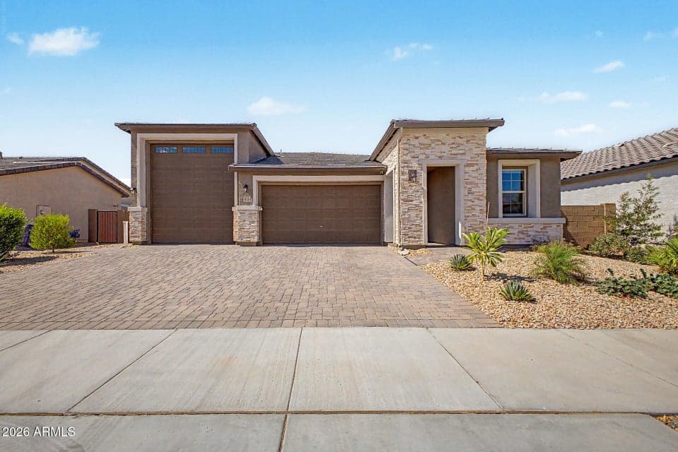 Stunning front elevation showcasing the home's modern architecture, stone-accent exterior, oversized 3-car RV garage, paver driveway, and low-maintenance desert landscaping. This beautifully designed home in Wittman offers exceptional curb appeal, mountain views, and a premium homesite backing to a natural wash with no homes behind.