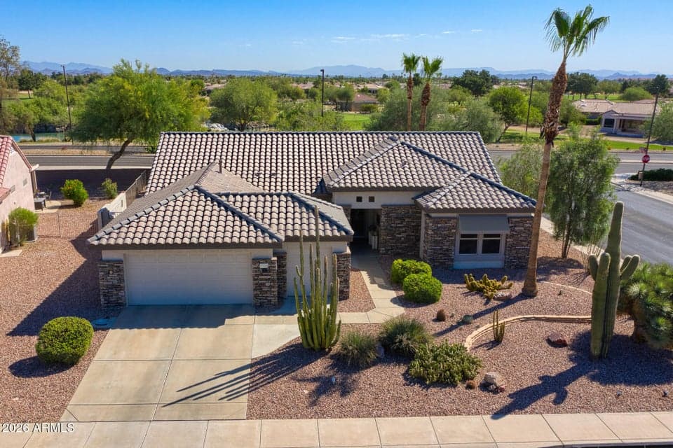 Beautiful front elevation of this meticulously maintained home in Surprise featuring stacked stone accents, desert landscaping, a spacious 2.5-car garage with golf cart parking, and stunning golf course surroundings. Recent updates including a new roof and modern finishes make this move-in-ready property a standout.
