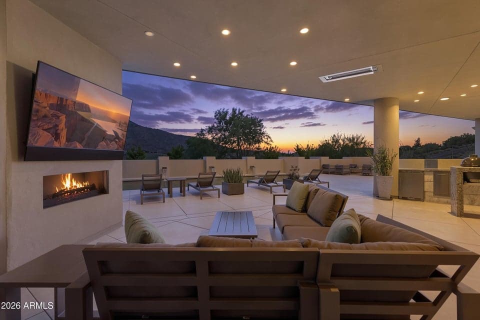 Twilight views from beneath a gracious outdoor living and dining room with charming fireplace, ceiling heaters, dining, grill, refrigerator, sink and snack storage