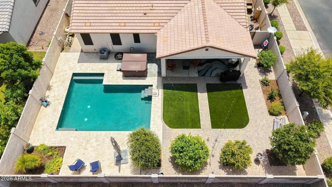 Aerial view showcases an impressive Avondale backyard with a sparkling swimming pool, above-ground spa, expansive covered patio, paved entertaining areas, landscaping, and green turf spaces designed for outdoor enjoyment.