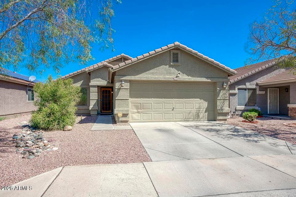 Single-story home with a tile roof, stucco exterior, and desert front landscaping. A security screen door covers the front entry, and the driveway leads to an attached 2-car garage.
