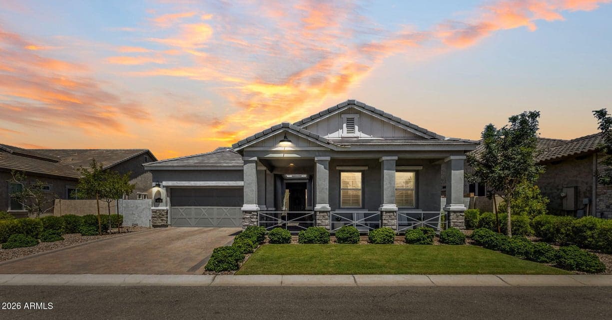 Beautiful front exterior of this move-in-ready Mesa home featuring a welcoming covered front porch, manicured landscaping, paver driveway, stone accents, and an attached garage. The polished exterior creates standout curb appeal beneath a dramatic Arizona sunset.